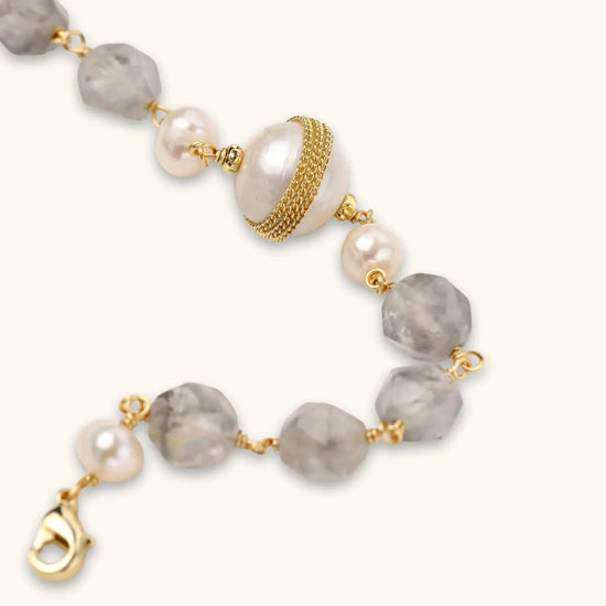 Bracelet with cloudy quartz beads, freshwater pearls, and gold-wrapped baroque pearl centerpiece on white background.
