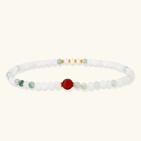 Three layered white beaded bracelets with carved orange agate lotus centerpiece and freshwater pearls on cream background.