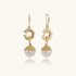 Gold sunburst charm earrings with baroque pearl drops on French hooks against cream background