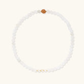 Three layered white beaded bracelets with carved orange agate lotus centerpiece and freshwater pearls on cream background.
