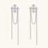 White gold plated baroque cross stud earrings with long cascading zirconia chains on cream background