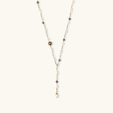 Y-shaped gold-plated necklace with white and gray freshwater pearls on cream background, showing adjustable drop design.