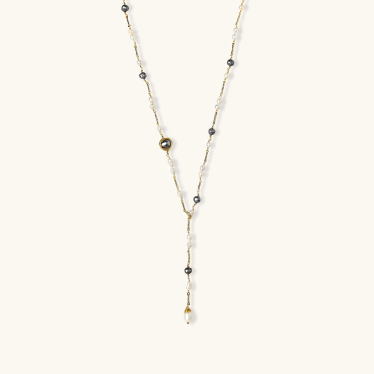 Y-shaped gold-plated necklace with white and gray freshwater pearls on cream background, showing adjustable drop design.