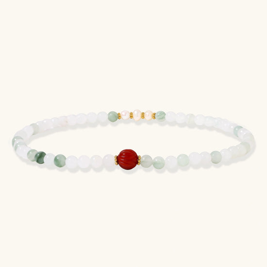 Three layered white beaded bracelets with carved orange agate lotus centerpiece and freshwater pearls on cream background.