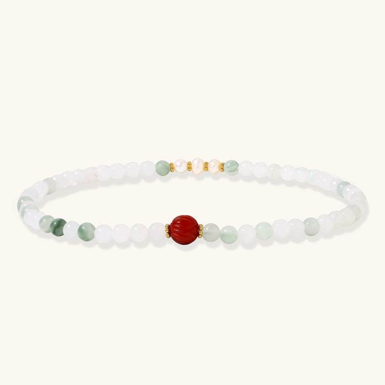 Three layered white beaded bracelets with carved orange agate lotus centerpiece and freshwater pearls on cream background.
